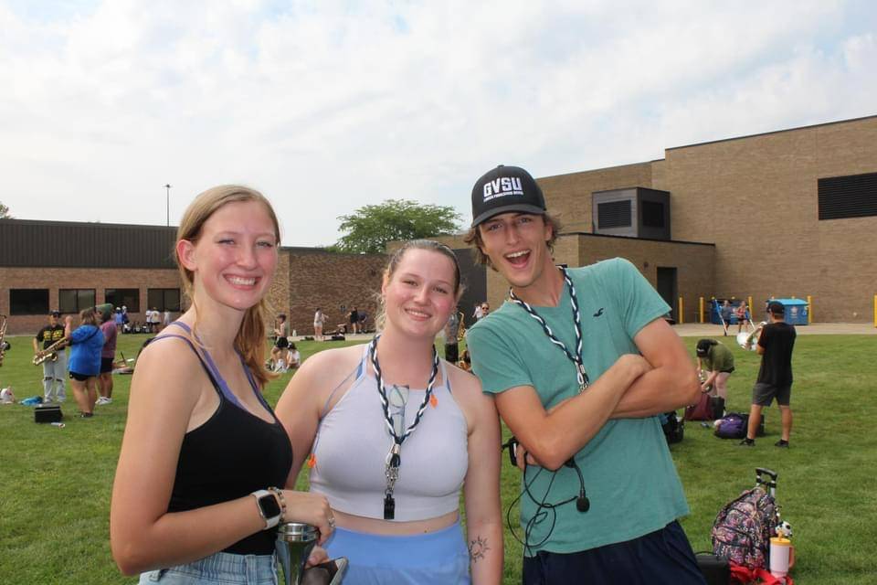 Three students standing outside in summer clothes smiling for a picture